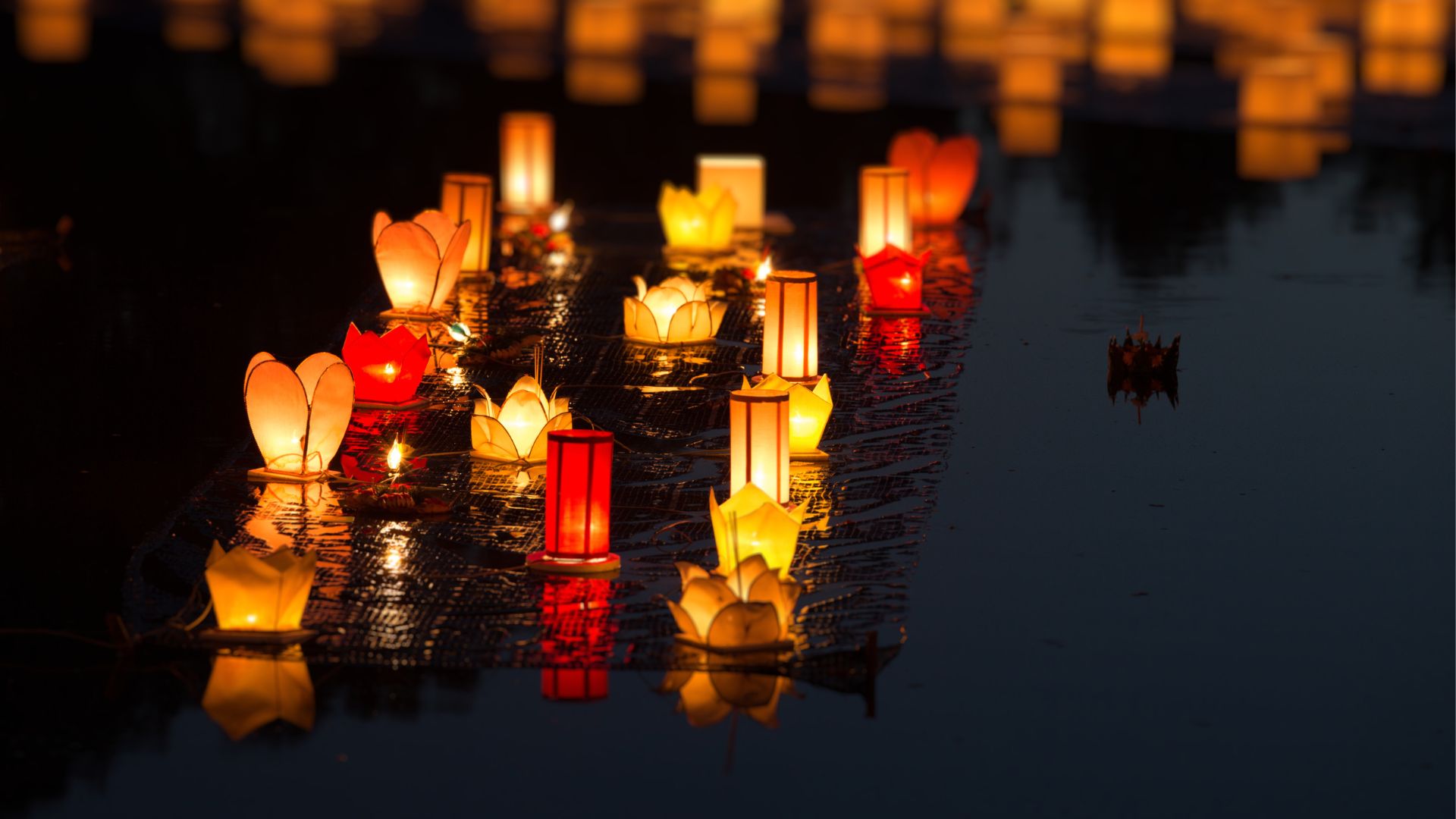 Glowing paper lanterns floating on dark water at night during an international cultural festival reached by private charter.